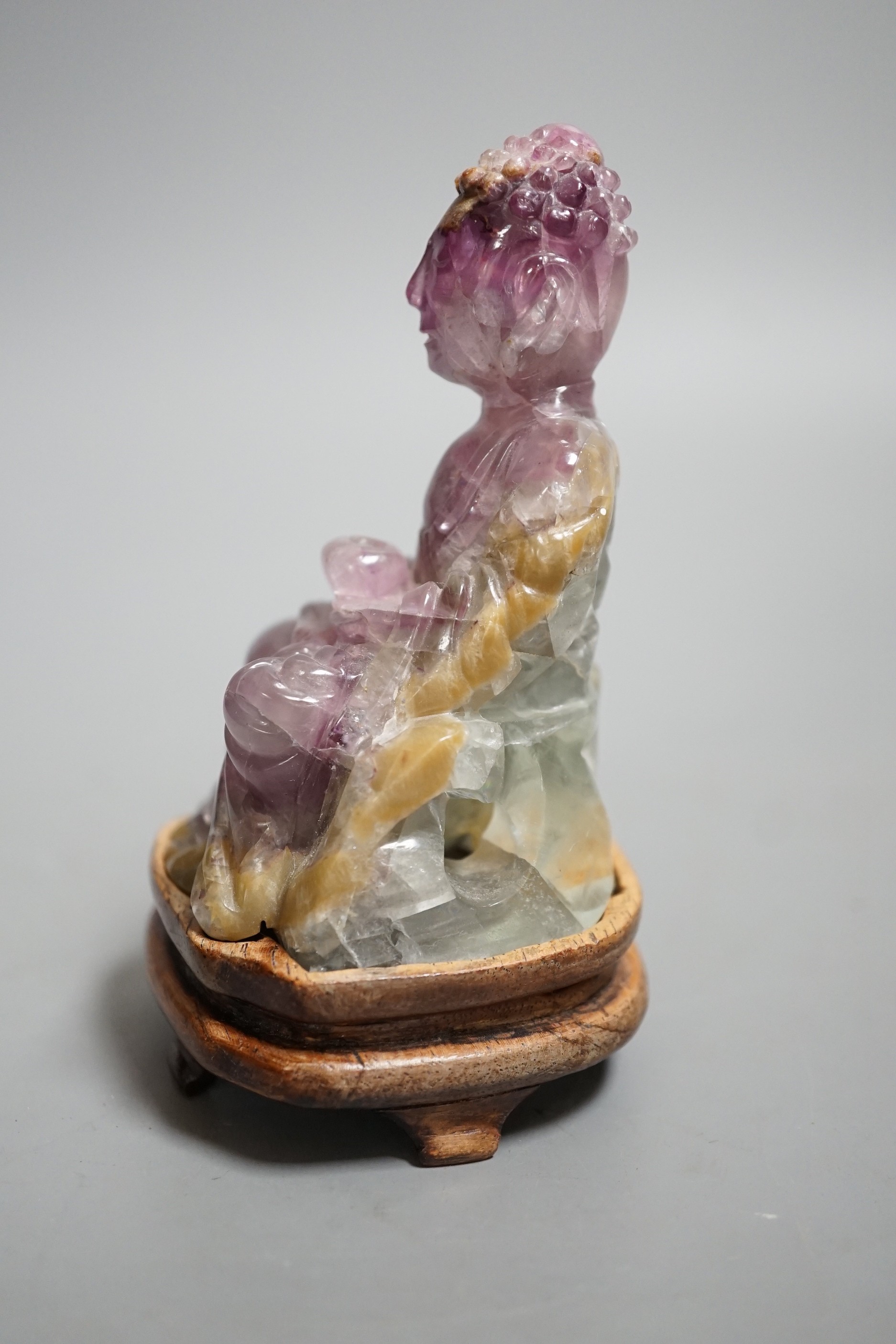 A 19th century amethyst and green quartz carving of a seated buddha on hardwood stand. Height 12cm